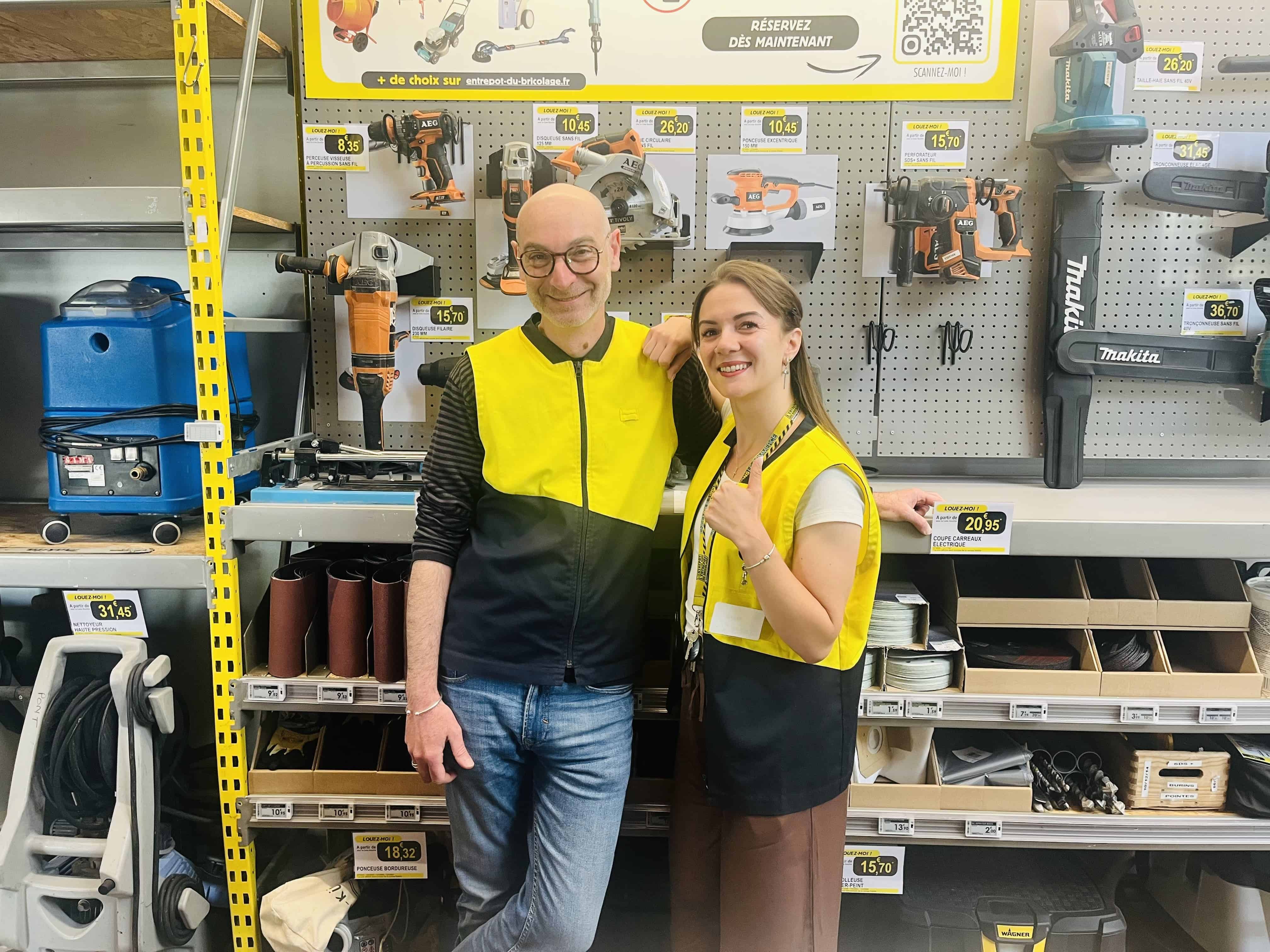 Deux employés souriants portant des gilets de sécurité dans un magasin de bricolage.